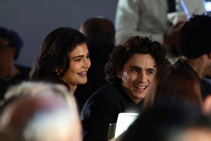 Two celebrities smiling and sitting together at a formal event