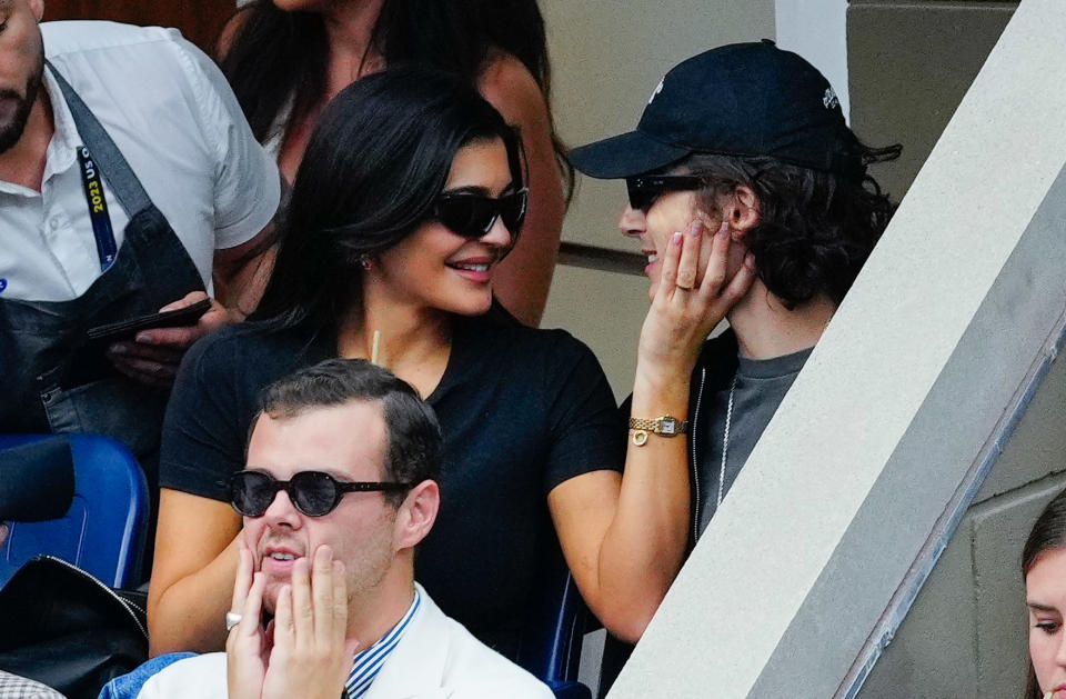 Kylie Jenner and Timothée Chalamet in casual attire smiling and touching faces at an outdoor event