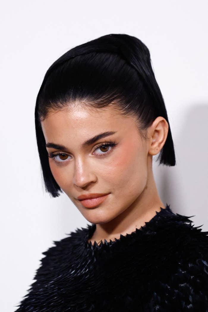 Person in a textured outfit with slick short hair poses for a portrait, gazing at the camera