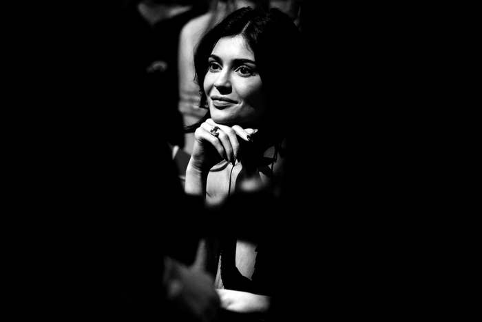 A person seated, looking thoughtful, wearing elegant attire with a sleeveless top. The image is in black and white, capturing a candid moment