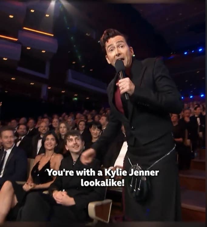 David Tennant in a black suit speaks to the audience at a seated event, captioned "You're with a Kylie Jenner lookalike!"