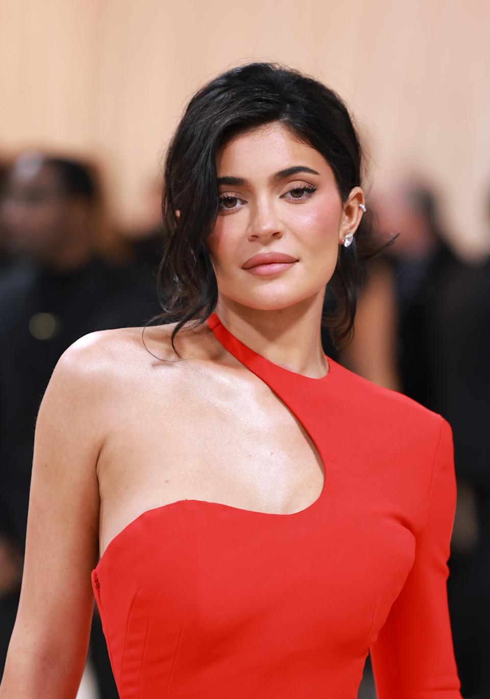 Kylie Jenner posing on a red carpet in an asymmetrical gown with one shoulder exposed