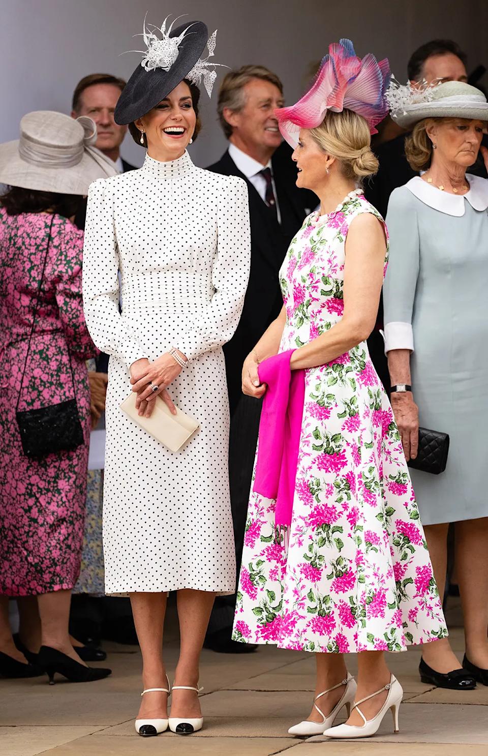Kate Middleton in a polka dot dress and a matching hat standing and laughing with Sophia in a floral dress and a matching pink hat.