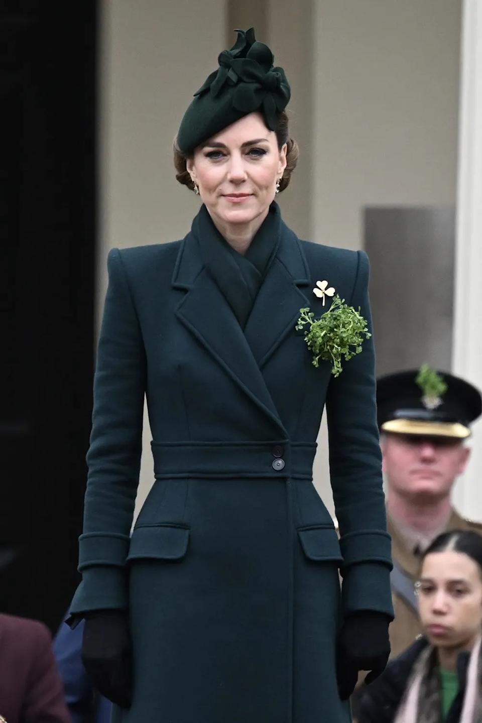 Kate Middleton standing in a fitted green coat with matching hat and shamrocks pinned to her.