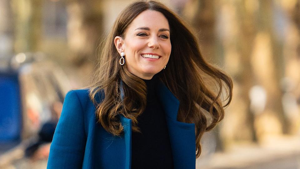 Kate Middleton smiling wearing a blue coat and a black sweater