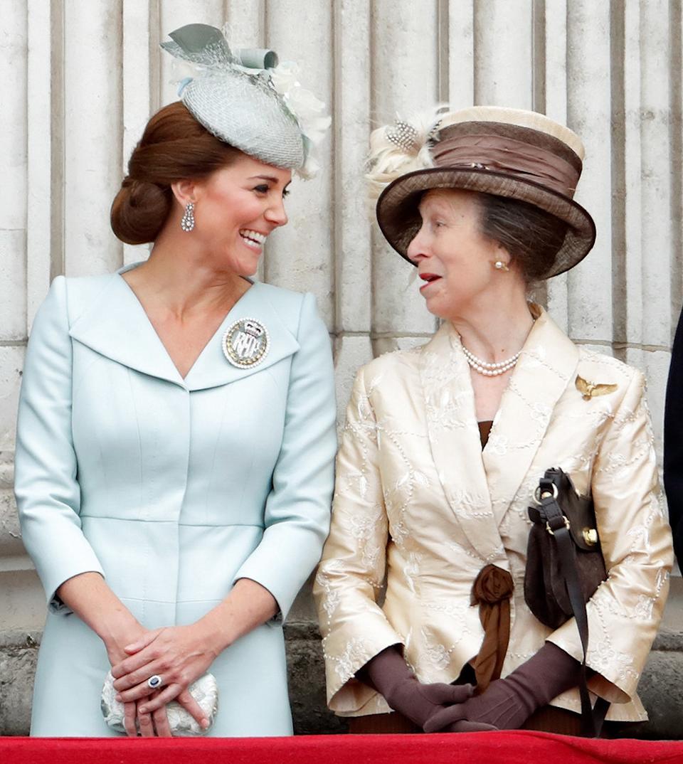 Kate Middleton wearing a pale blue dress smiling at Princess Anne wearing an ivory dress with a matching brown hat.