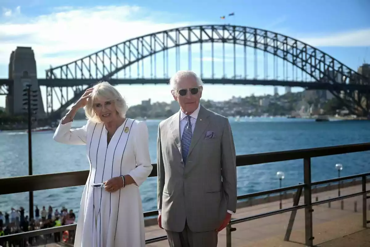 Camilla Parker and Charles III posing in front of the iconic Sydney Bridge on a sunny day.