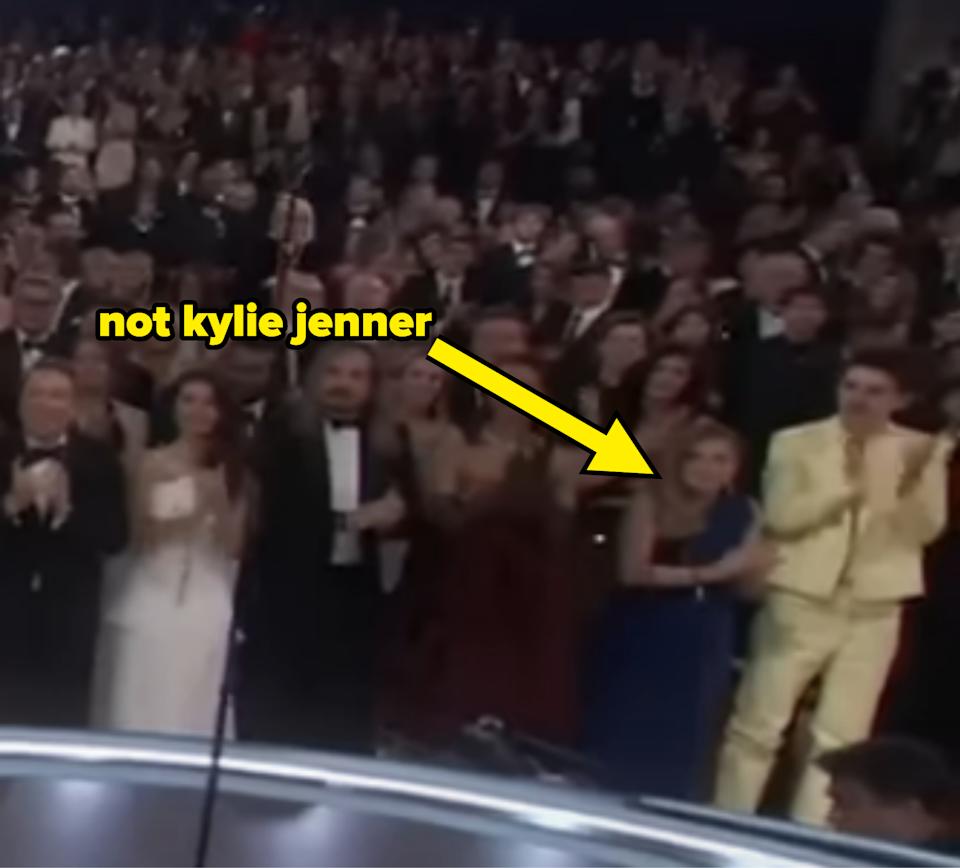 A crowd stands at an event, with an arrow pointing to a person labeled "not kylie jenner." The audience is applauding