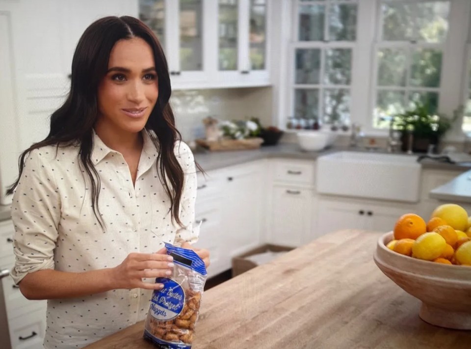 Meghan Markle holding a bag of pretzels in a kitchen.