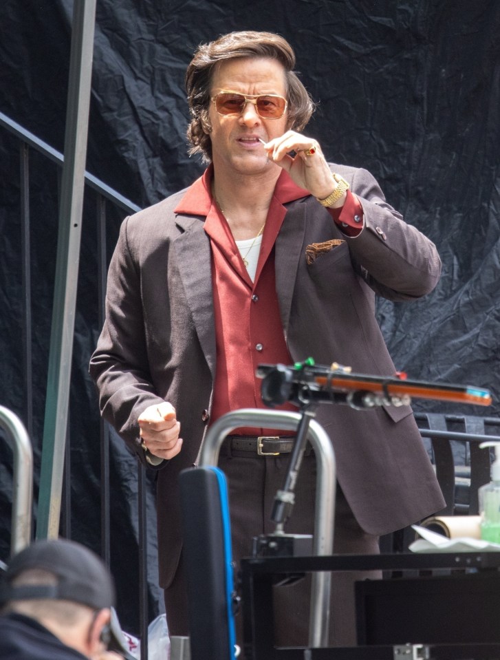 Mark Wahlberg on the set of "By Any Means," wearing a brown suit and sunglasses.
