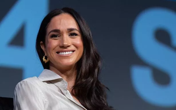 Meghan Markle in a grey shirt on a stage.