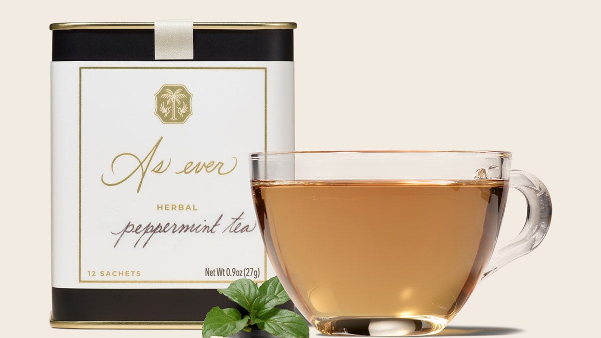A clear glass of peppermint tea next to a container
