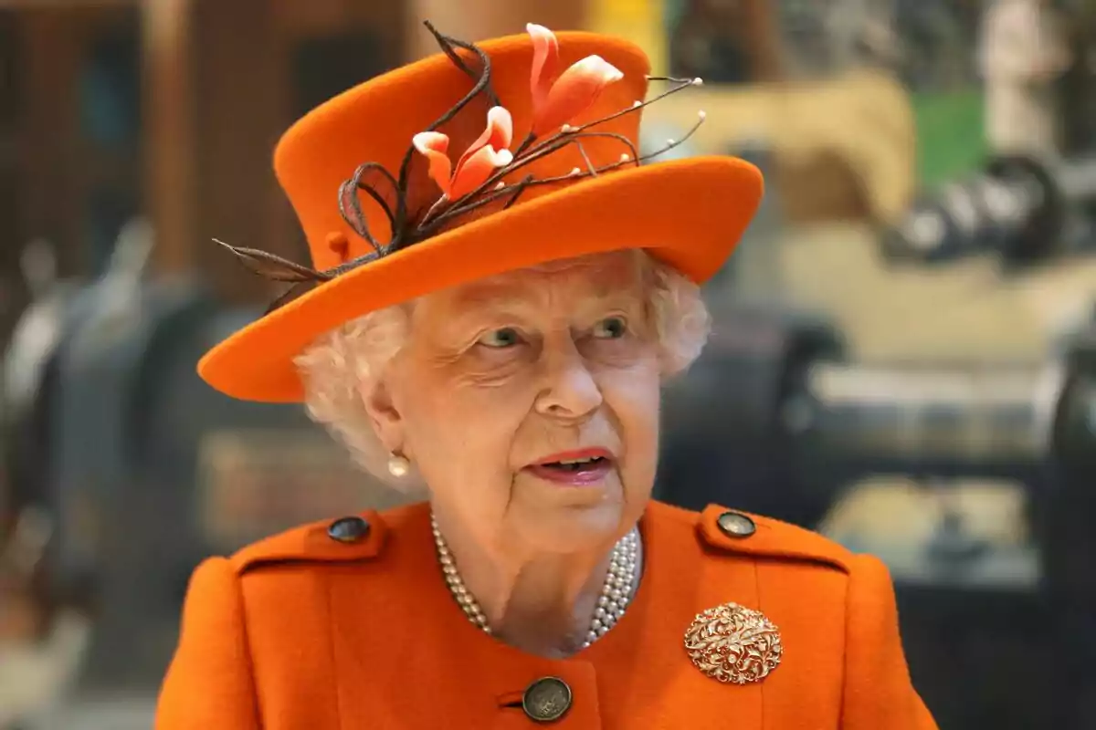 An elderly person with a hat and an orange coat adorned with flowers and a brooch.