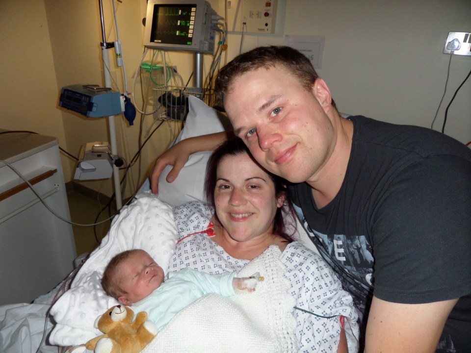 Parents holding their newborn baby in a hospital bed.