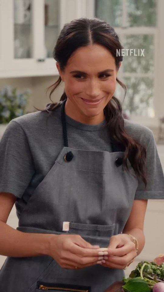 Meghan Markle in a gray apron, smiling.