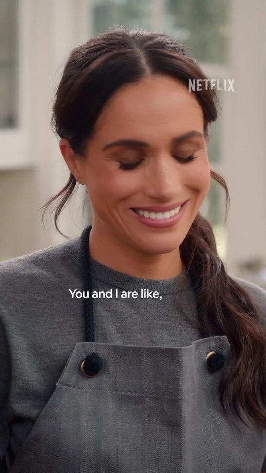 Meghan Markle smiling and wearing an apron.