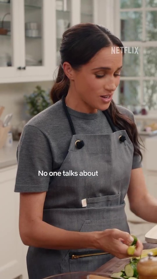 Meghan Markle in a gray apron preparing cucumbers.