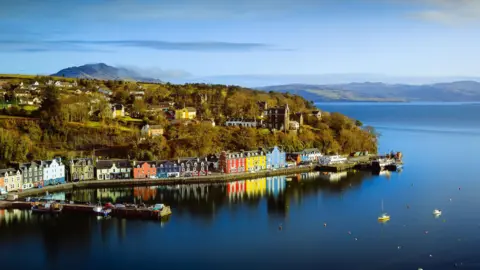 Getty Images Landscape aerial view looking down on the colourful seafront houses on the isle of Mull with sea and mainland on the horizon behind.