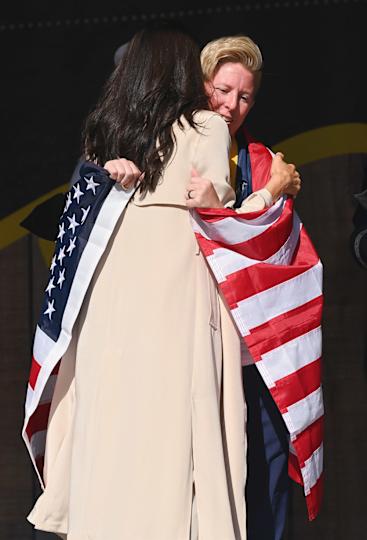Meghan Markle hugging a woman with an American flag wrapped around them.