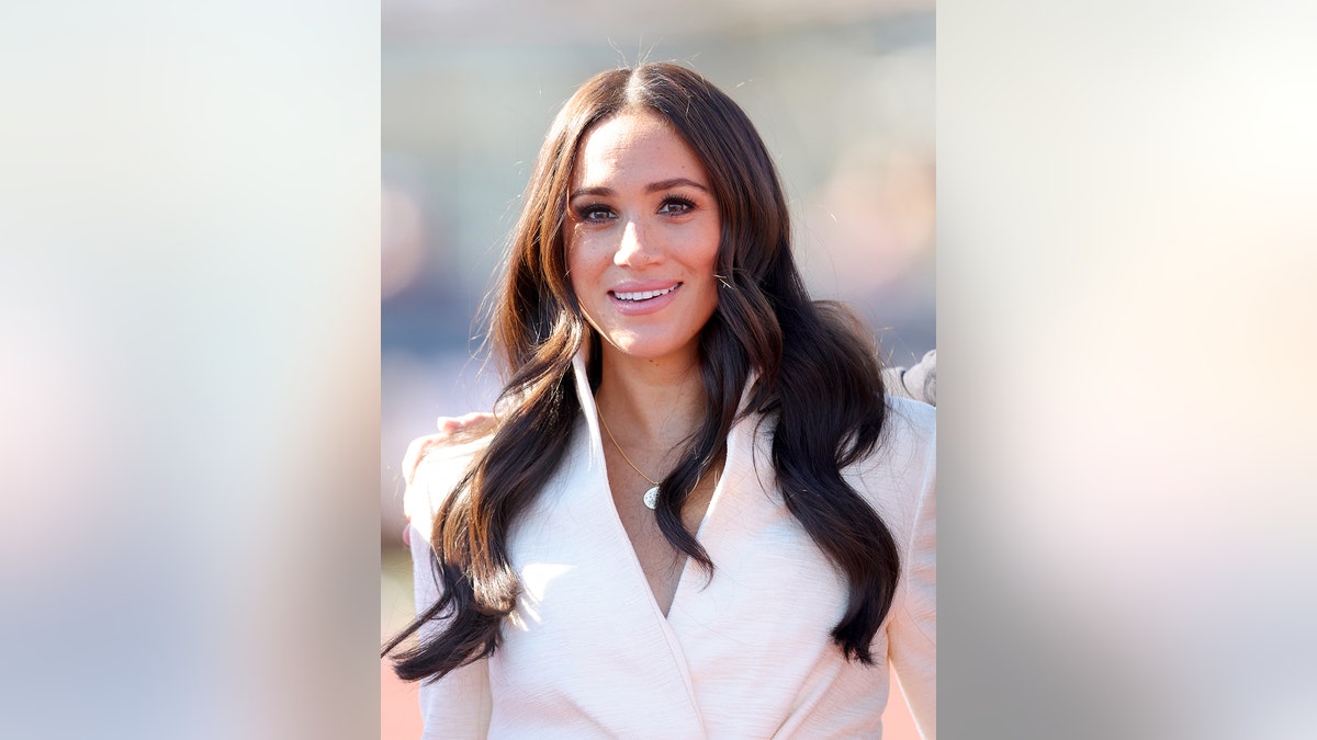 Meghan Markle smiling wearing a white suit with her hair down.