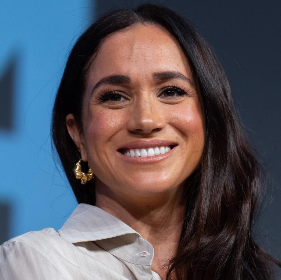 Meghan Markle smiling and wearing gold hoop earrings and a collared blouse .