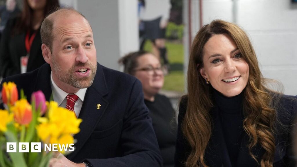 William and Kate celebrate anniversary on Isle of Mull William and Kate sitting next to each other and smiling while talking to someone off camera - William has a dark suit and red tie on, while Kate has a dark blue jacket on. Flowers sit in front of the couple.