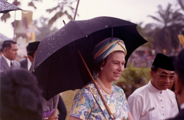 Britain’s Queen Elizabeth II is pictured sheltering under an umbrella...