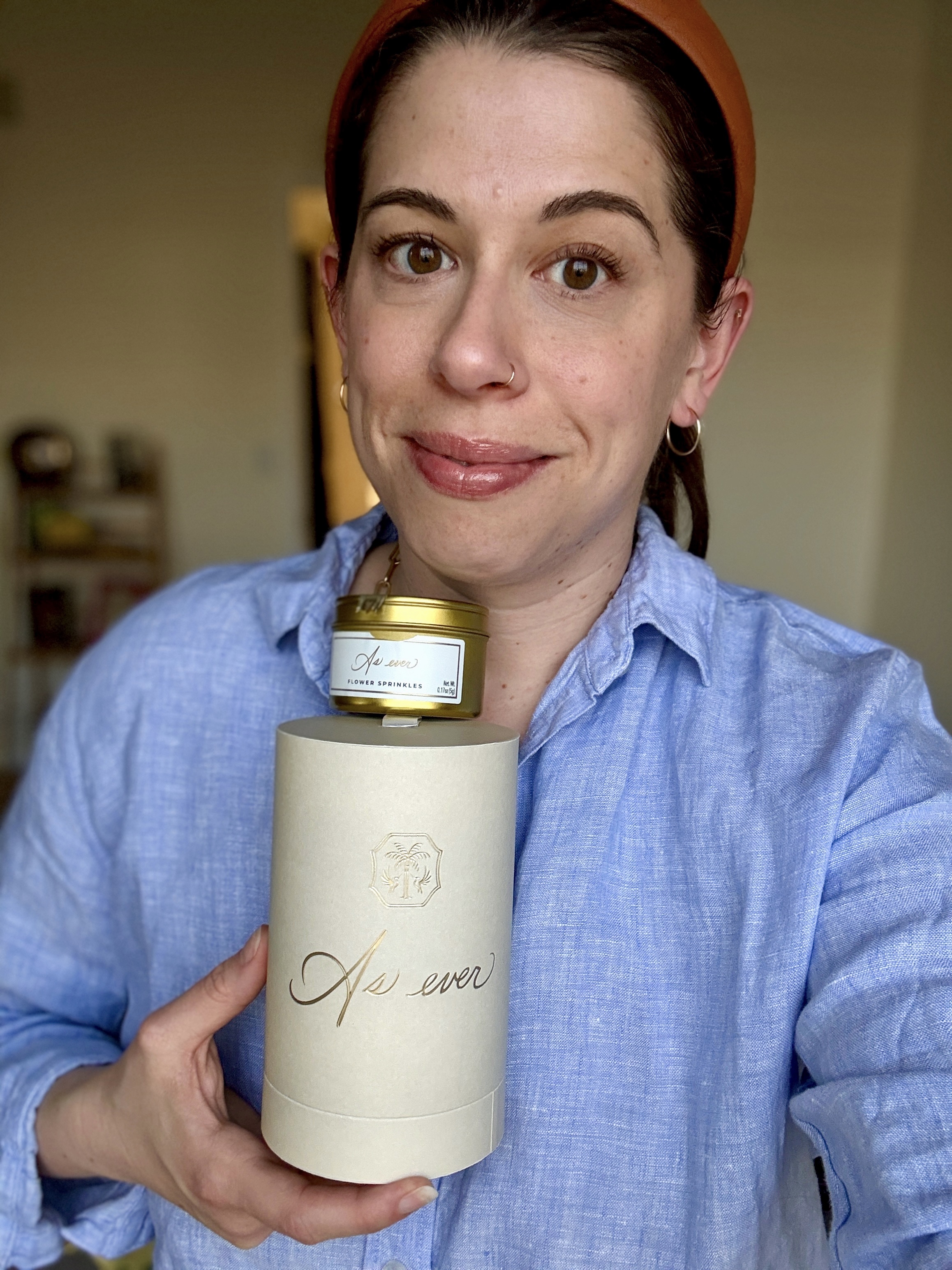 A woman wearing a chambray shirt holding a package of As ever jam and flower sprinkles