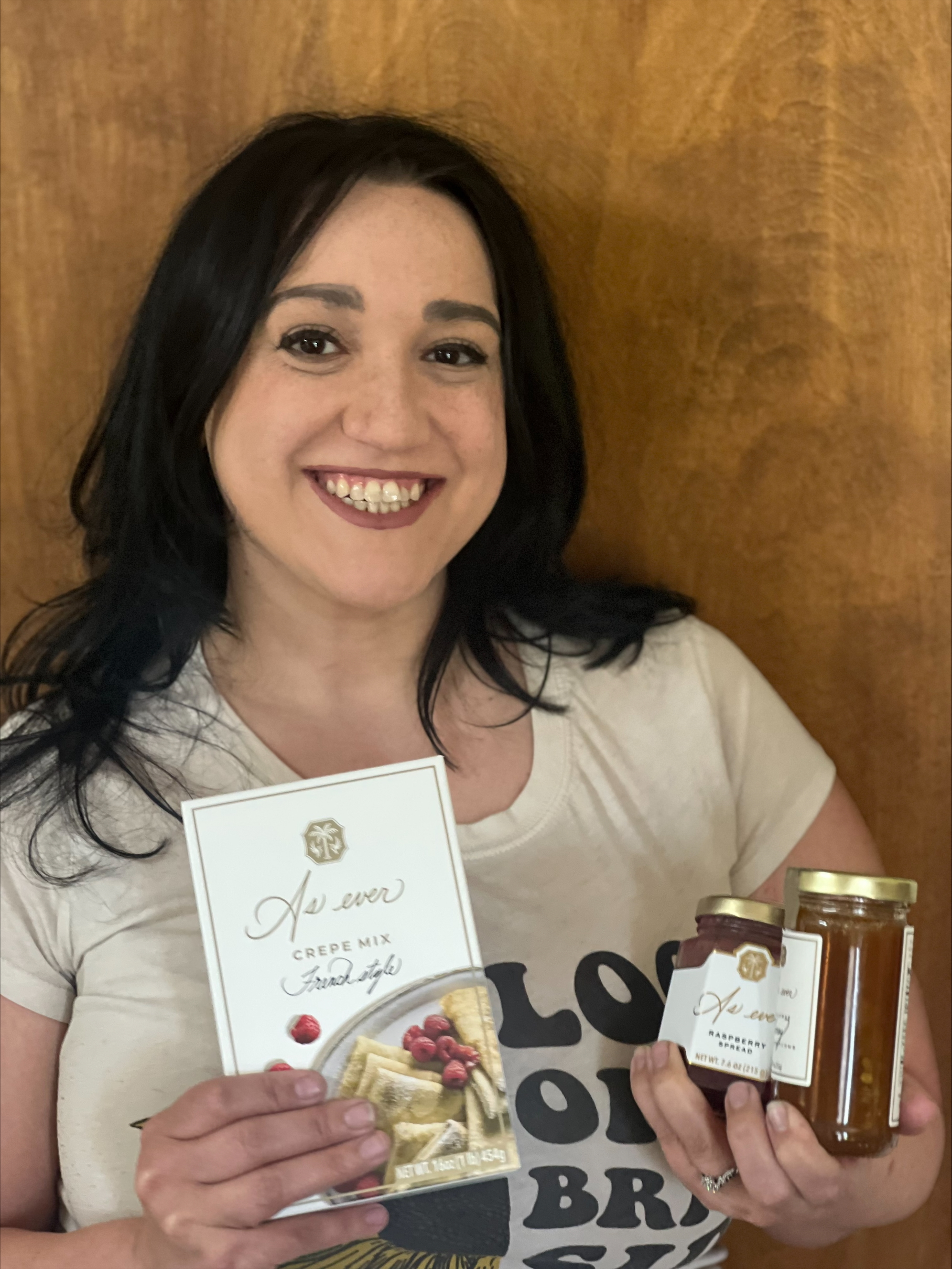 A woman smiling and holding As ever crepes, honey and jam