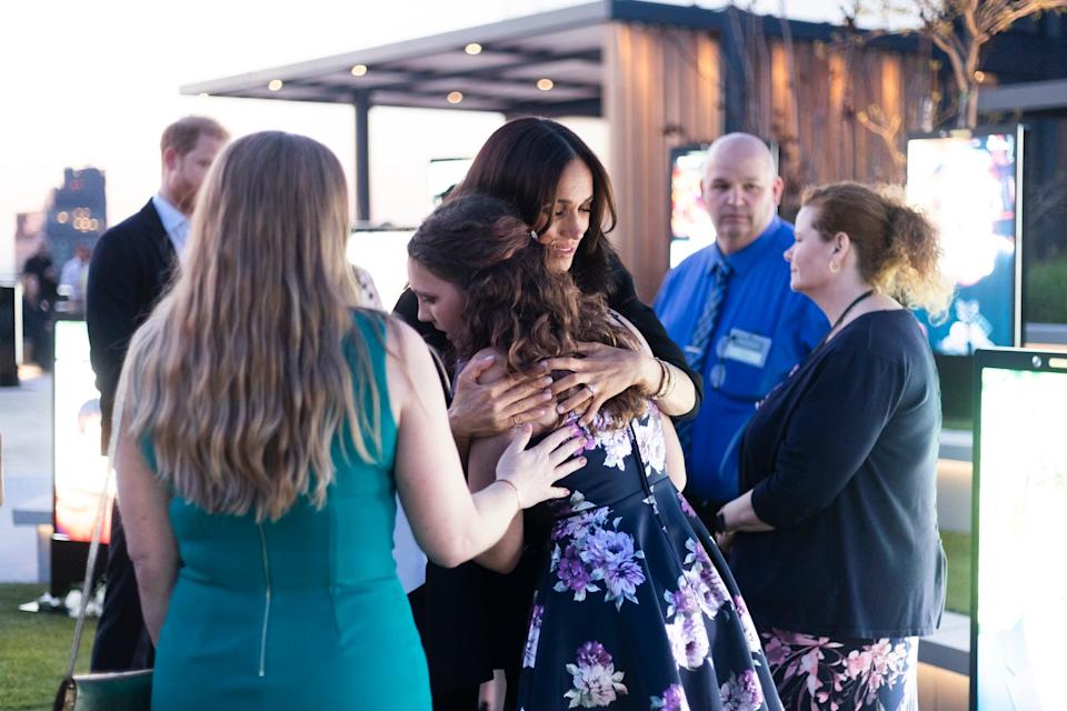 Meghan Markle hugs a girl while other people stand around them.