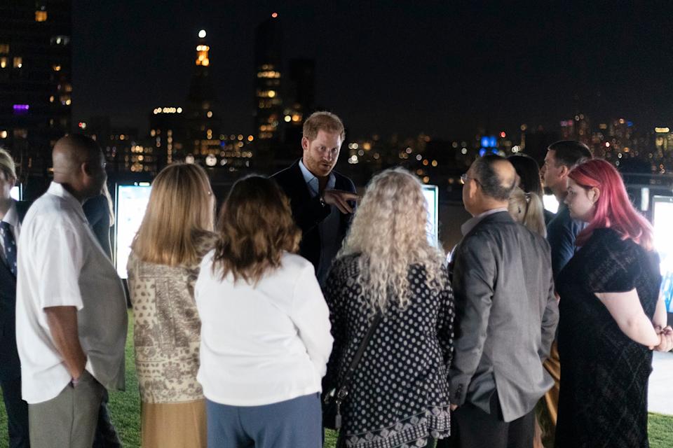 Prince Harry speaks to a group of people on a rooftop.