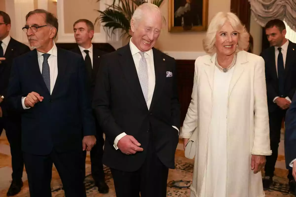 A group of formally dressed people smiles and chats at a social event in an elegant interior. A group of formally dressed people smiles and chats at a social event in an elegant interior.