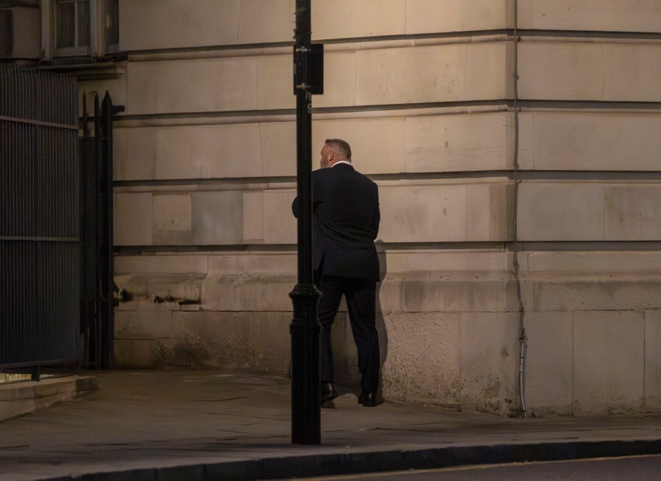Wayne Rooney standing against a wall at night.