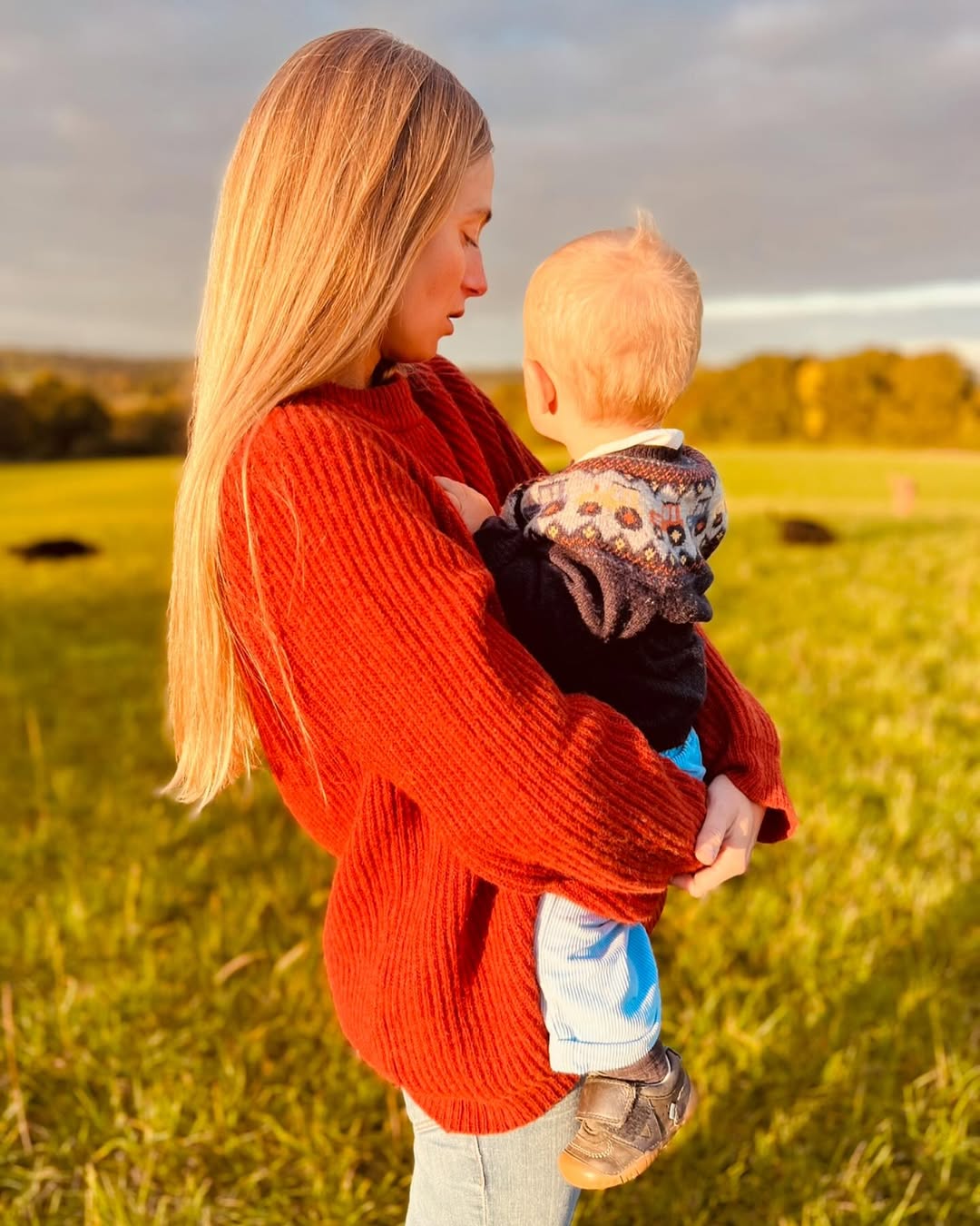 Alizee Thevenet wearing a red sweater holding her son Inigo in a field