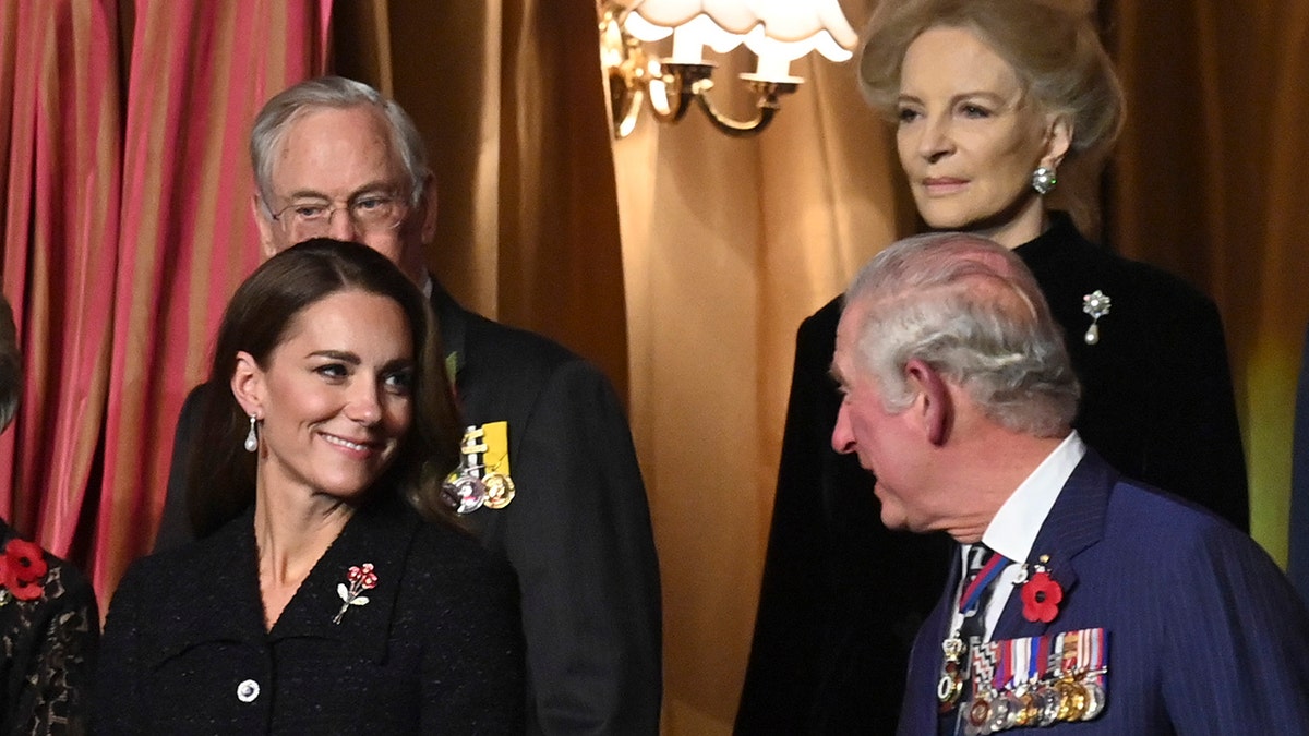 Kate Middleton in a dark suit smiling at King Charles wearing a dark blue suit with medals.