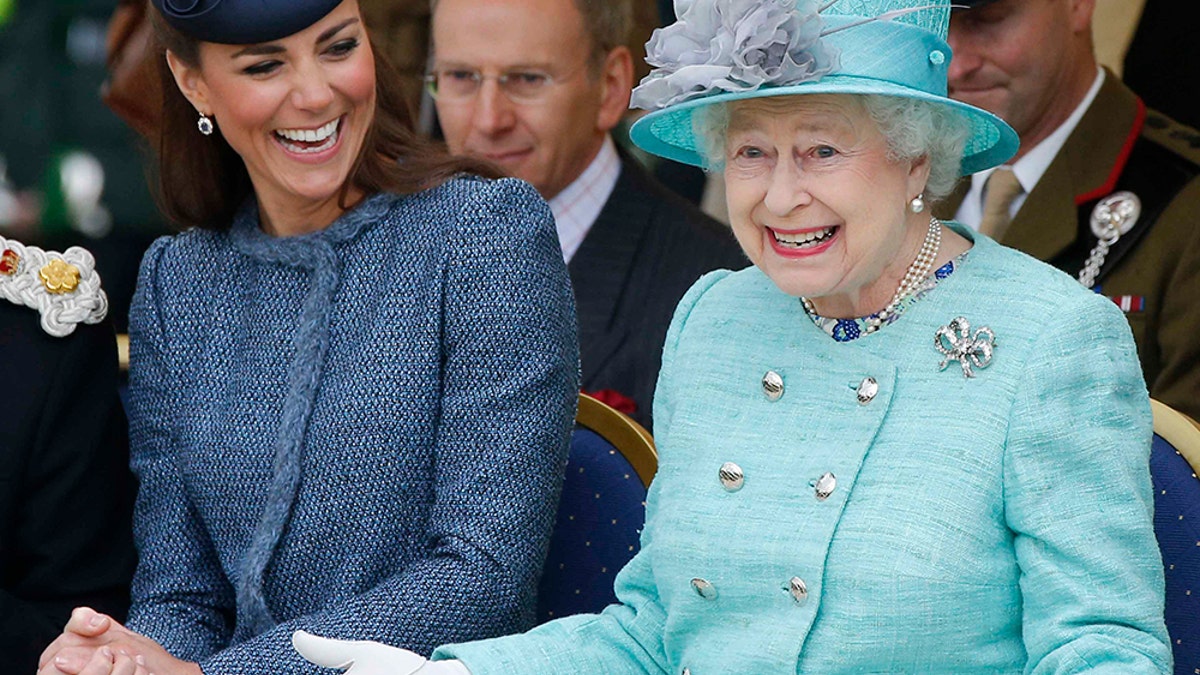 Kate Middleton with a dark blue suit and matching hat sitting next to Queen Elizabeth II who is wearing a light blue suit with a matching hat.