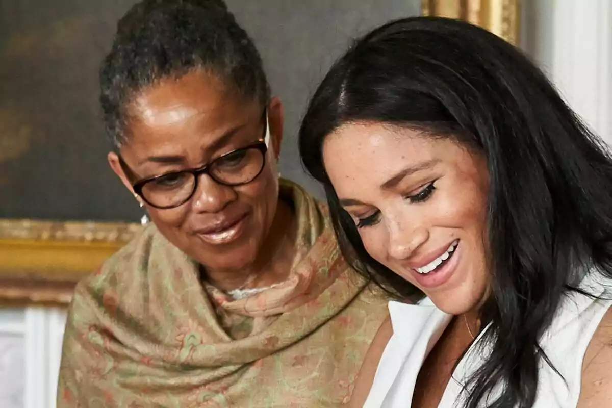 Two women smile while looking at something together.