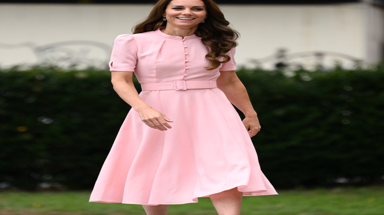 Kate Middleton walking and smiling in a pink dress with her hair half over her shoulder