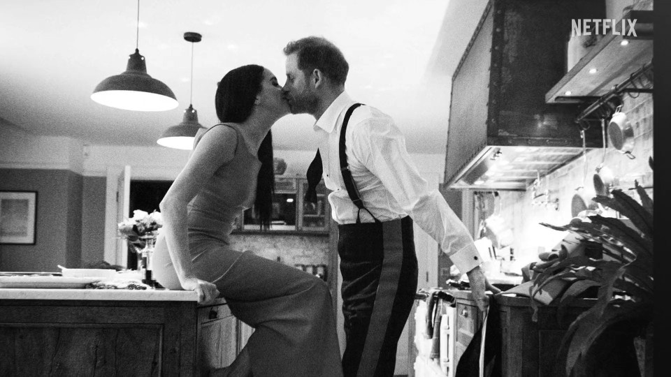Black and white image of Meghan Markle and Prince Harry kissing in a kitchen.