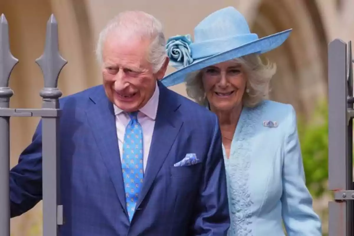 King Charles III and Queen Camilla smile as they walk together, one wearing a blue suit and the other a light blue dress and hat. King Charles III and Queen Camilla smile as they walk together, one wearing a blue suit and the other a light blue dress and hat.
