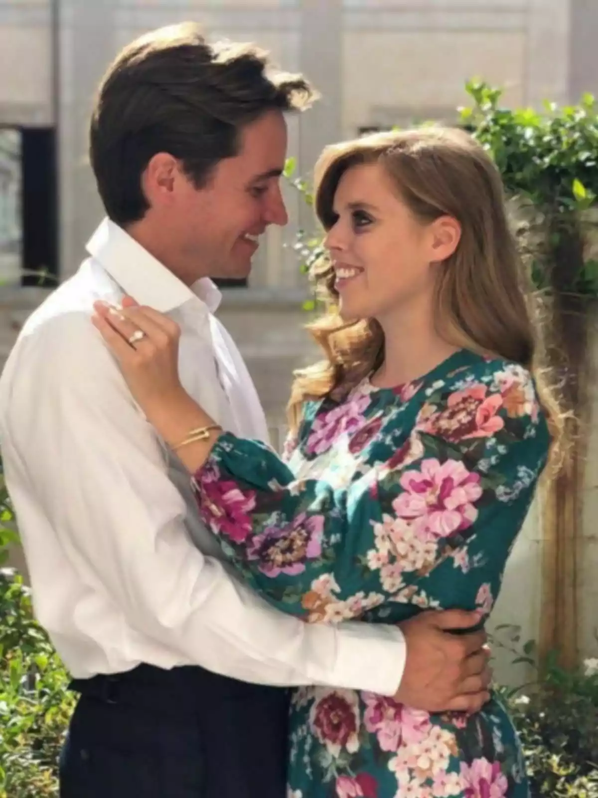 Edoardo Mapelli and Beatrice of York smile at each other while embracing in an outdoor setting with vegetation.