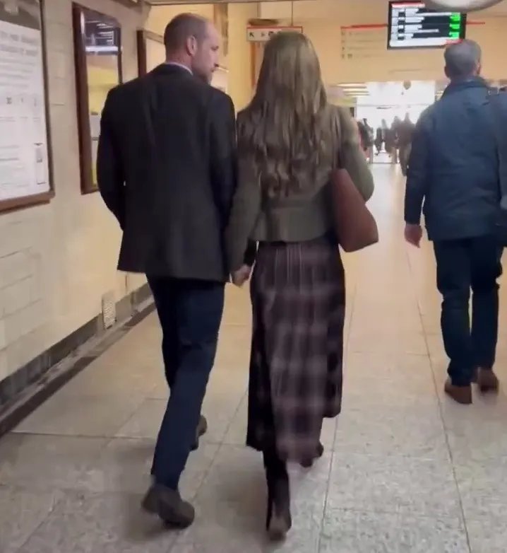 The Prince and Princess of Wales holding hands and walking down a hallway.