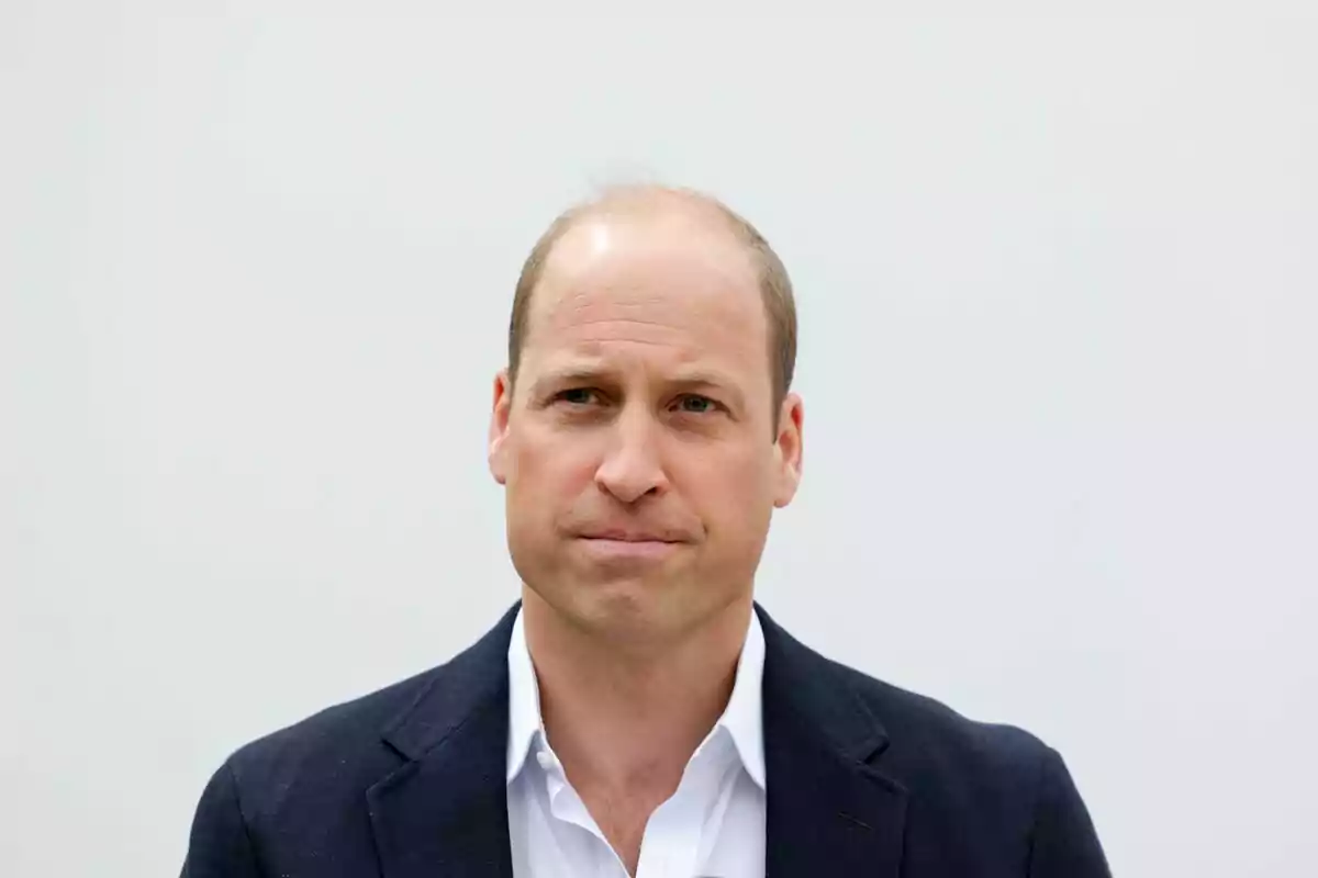 Prince William in a dark jacket and white jersey against a light background.