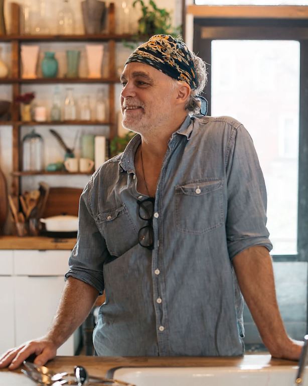 Man in denim shirt and bandana leaning on kitchen counter.