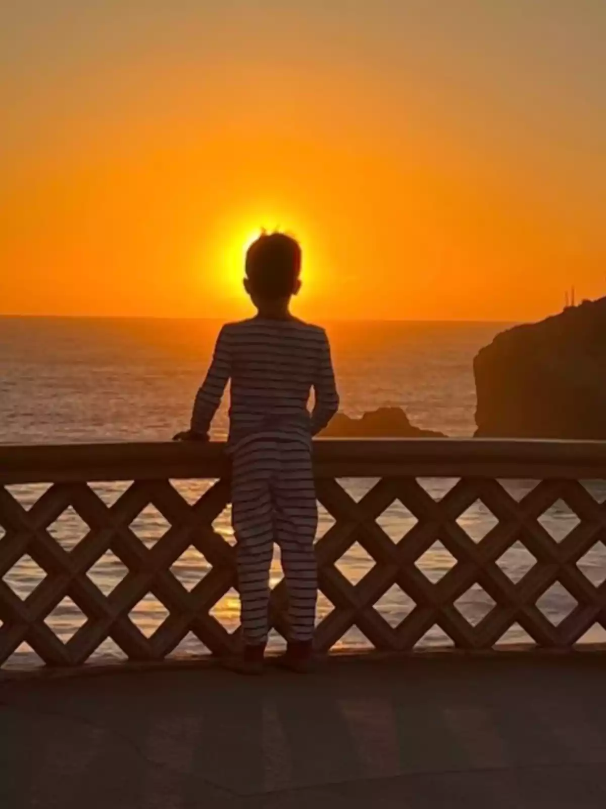 Archie in striped pajamas watches the sunset from a balcony overlooking the sea.