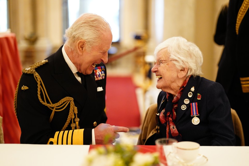King Charles III and a veteran laughing together at a tea party.
