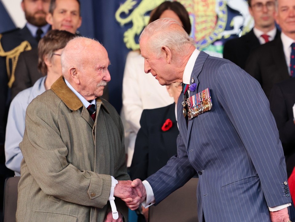 King Charles III shaking hands with a veteran at a VE Day anniversary event.