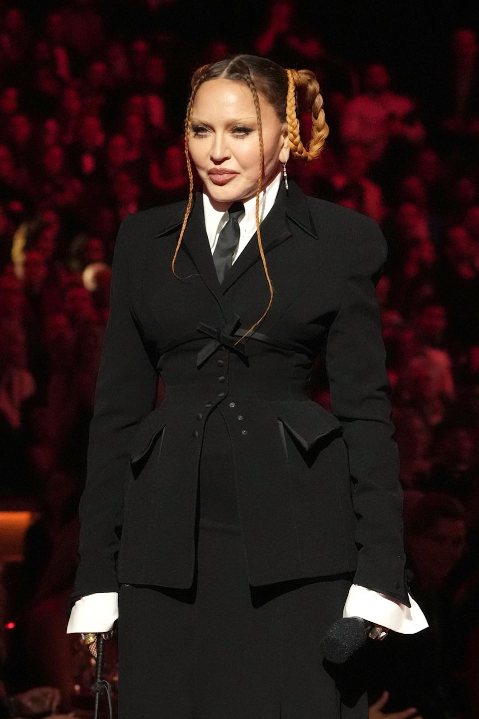 Madonna in a structured black suit and braided hairstyle, standing in front of people at the Grammys