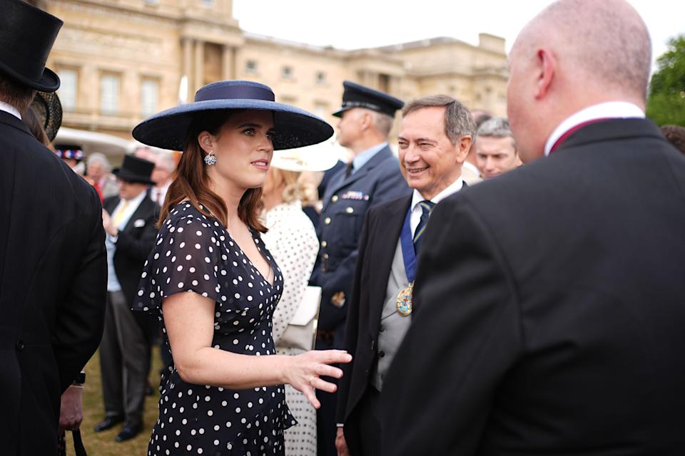 Princess Eugenie in a navy polka dot dress talking to men at a garden party