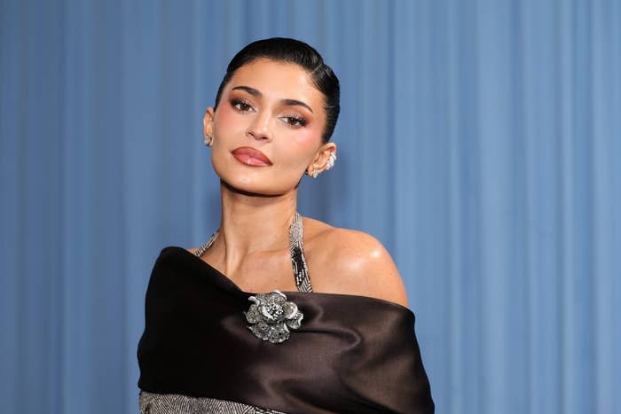 Kylie Jenner posing on a red carpet, wearing an elegant off-shoulder gown with sparkling embellishments and a sophisticated updo hairstyle